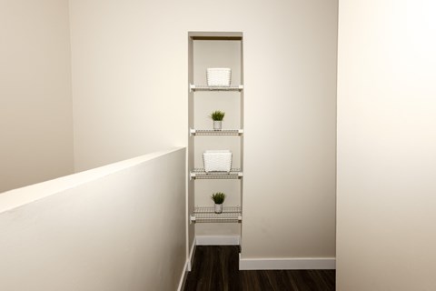 A white shelf with three shelves holding a plant and a white bowl.