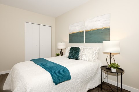 A bedroom with a white bed and a painting on the wall.