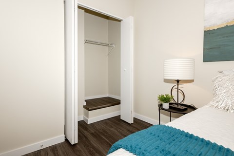 A bedroom with a bed, a nightstand with a lamp, and a closet with a bench.