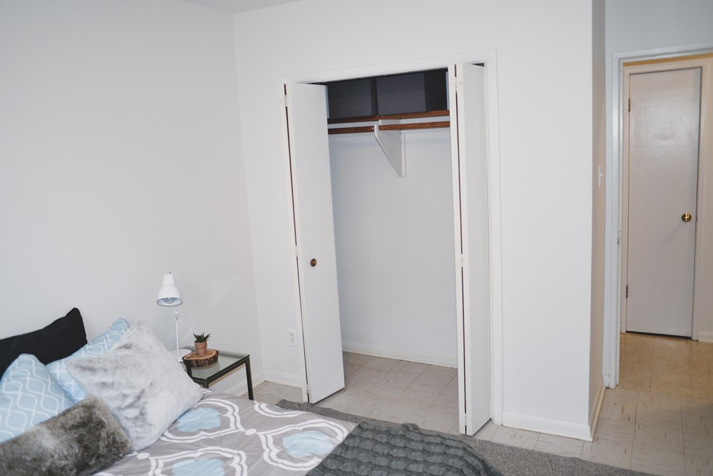 A white bedroom with a bed, pillows, a nightstand, and a closet.