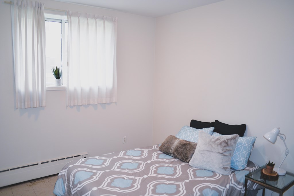 A bedroom with a bed, pillows, and a small table with a lamp.