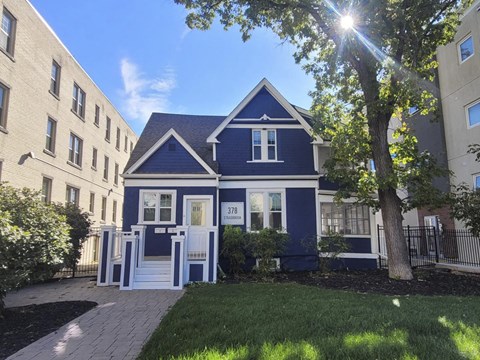 A blue house with white trim and a white door is in front of a tall building.
