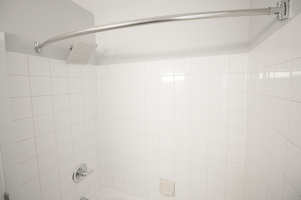 A white tiled shower with a silver shower head and hand held shower.