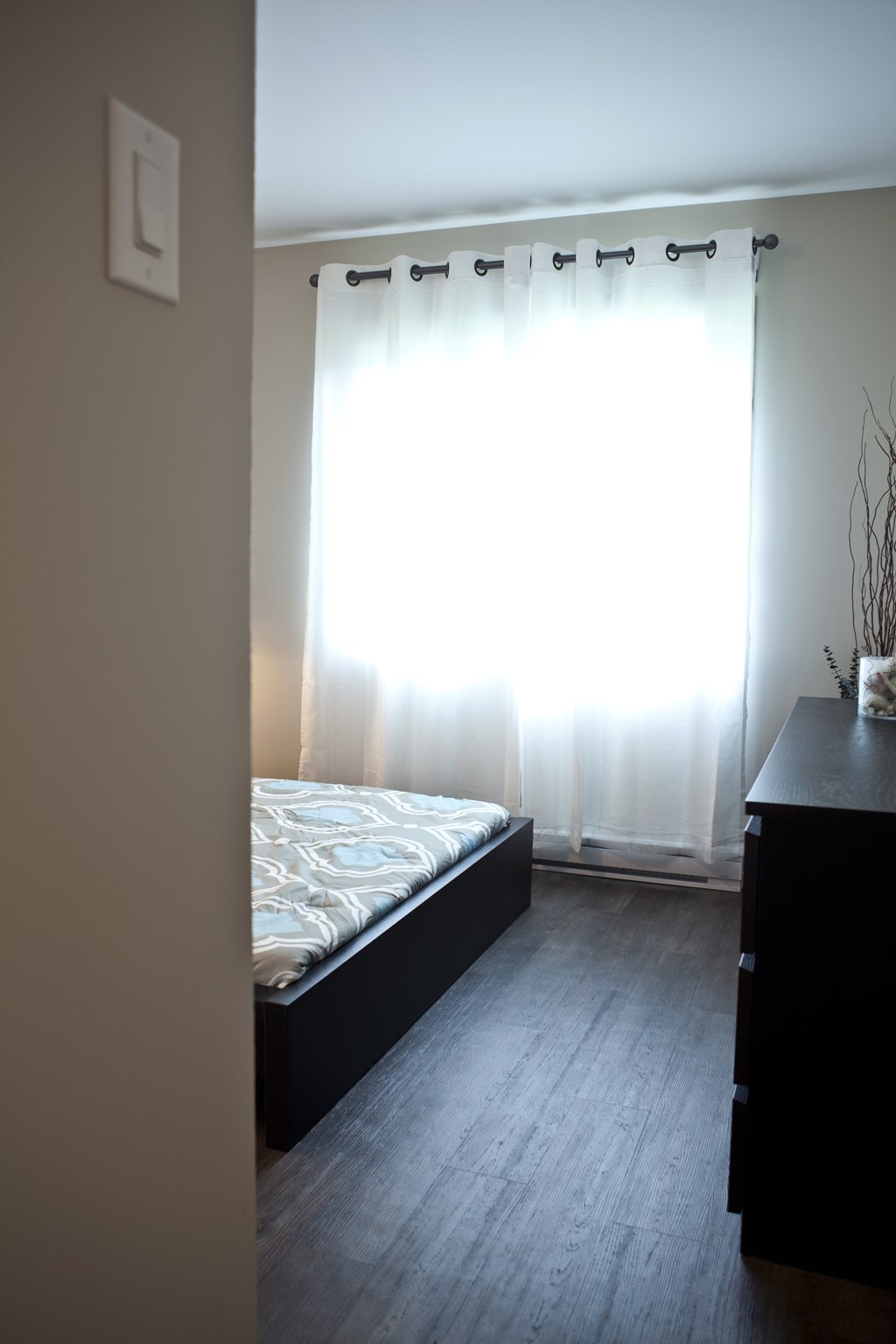 A bedroom with a bed, dresser, and window with curtains.