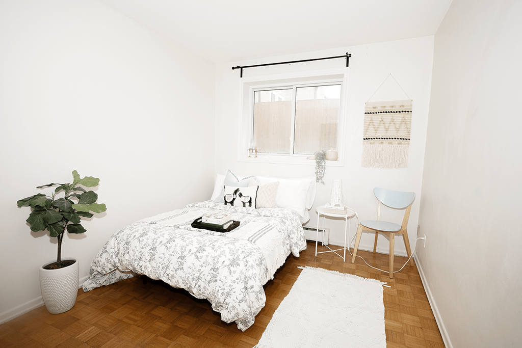 A white bedroom with a bed, chair, and potted plant.
