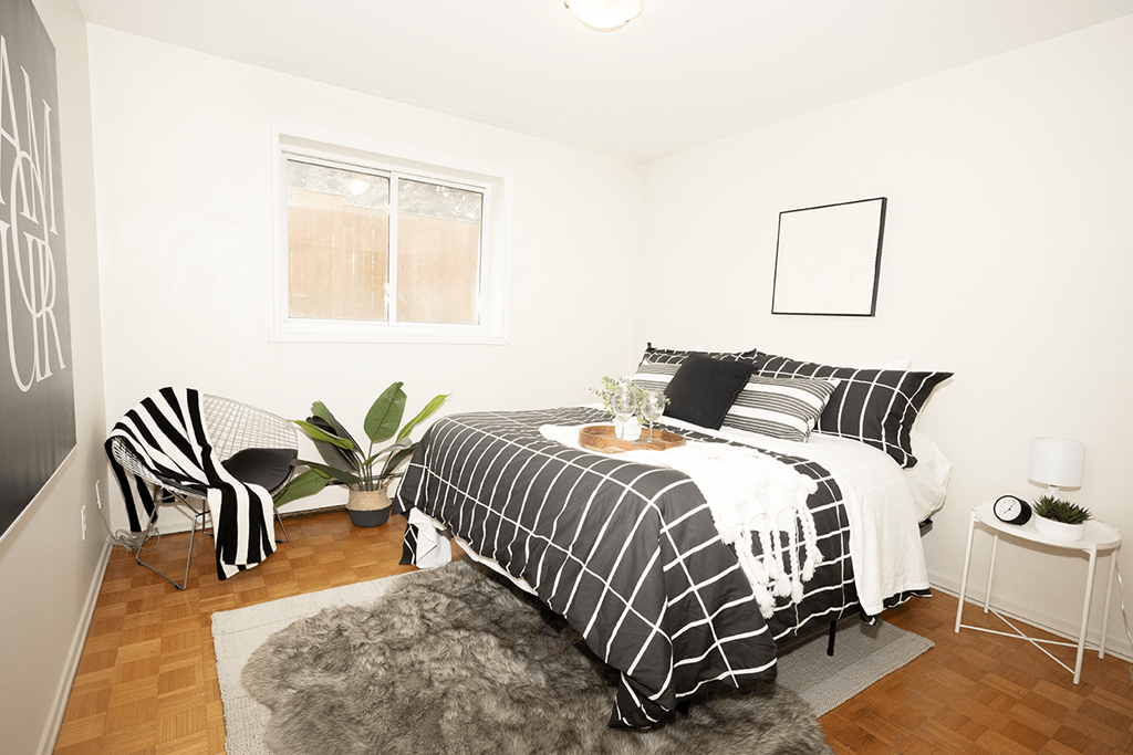 A bedroom with a bed, chair, and plant.