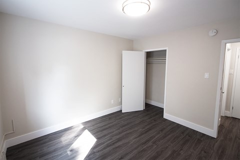 a bedroom with white walls and wood flooring and a closet