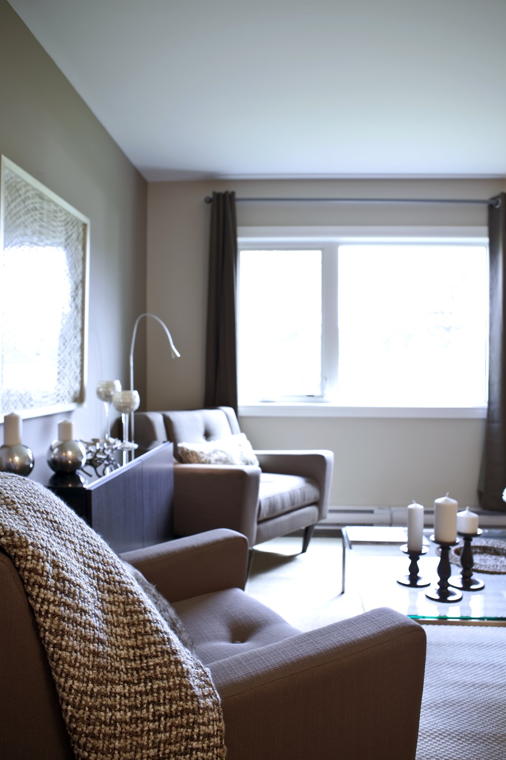 A living room with a couch, a chair, a table with candles, and a window.