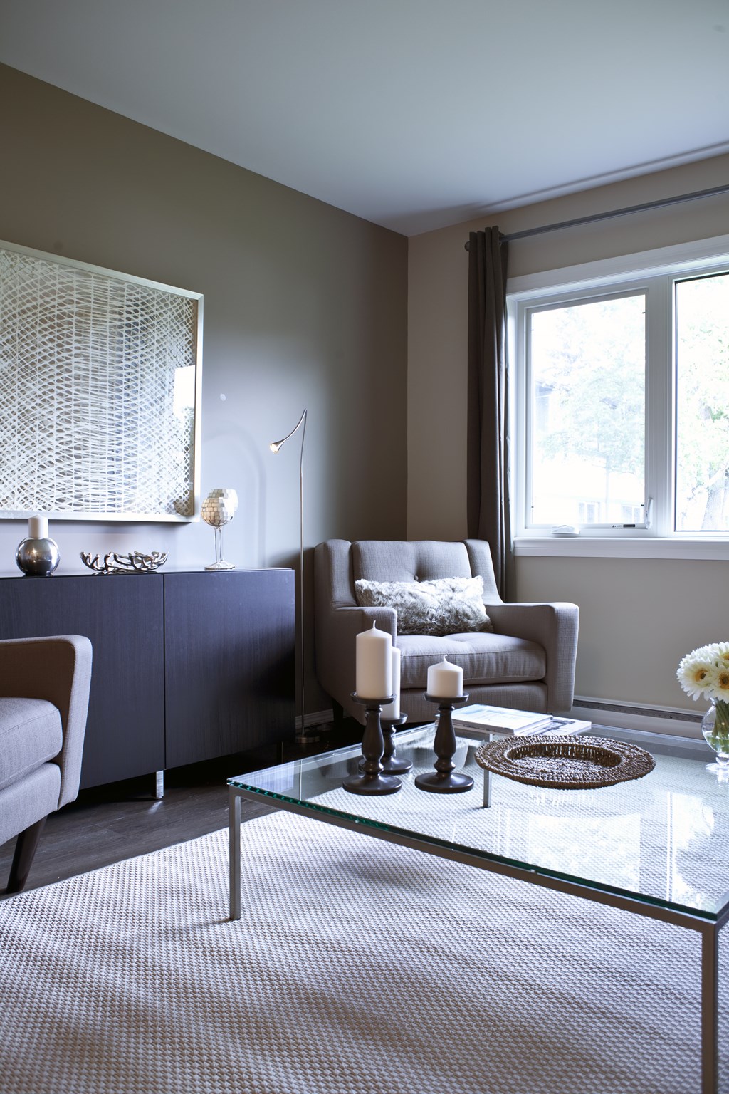 A living room with a glass coffee table and a grey sofa.
