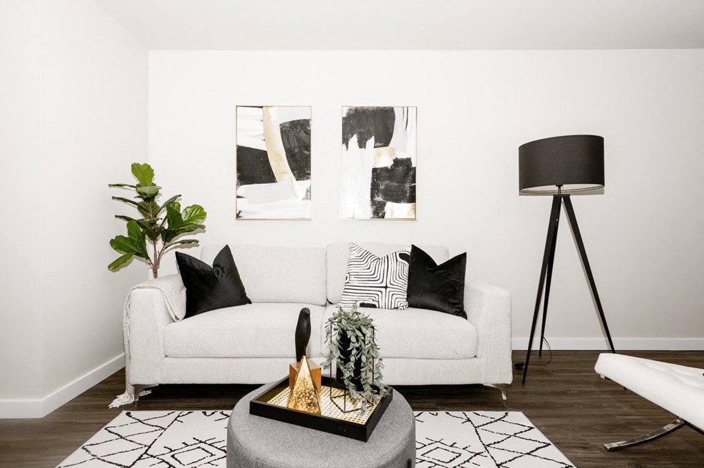 A white couch with a black and white pillow is in front of a wall with two paintings on it.