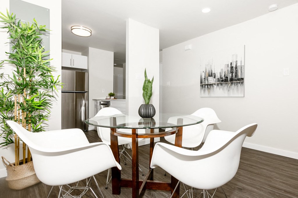 A modern dining room with a glass table and white chairs.