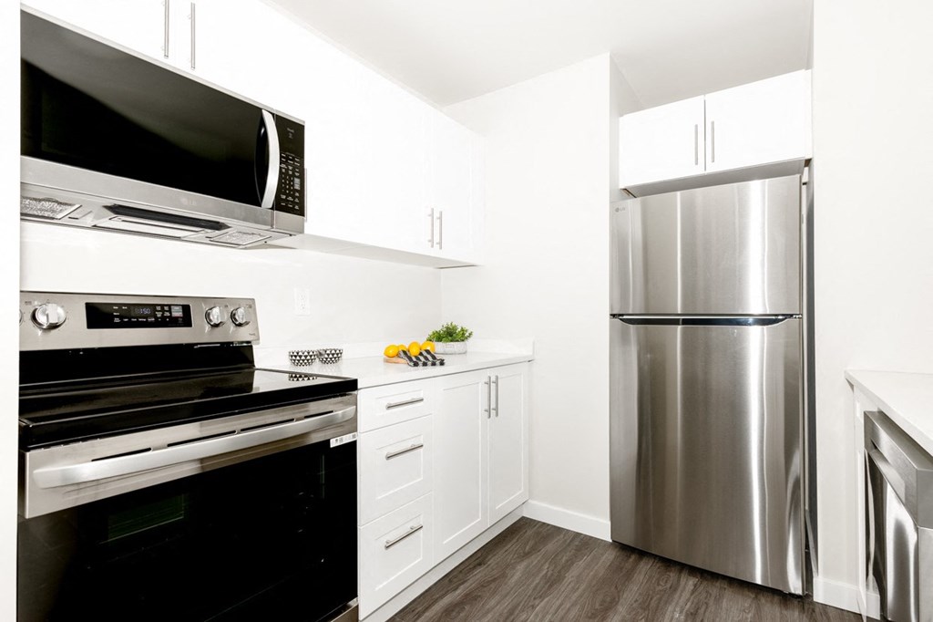 A modern kitchen with a stainless steel refrigerator, black oven, and white cabinets.