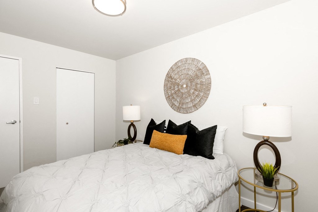 A bedroom with a bed, two lamps, and a wall hanging.