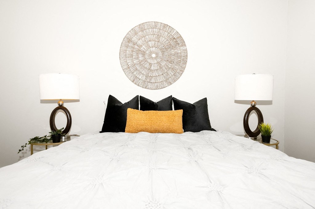 A bed with a white comforter and a yellow pillow is flanked by two lamps on side tables.