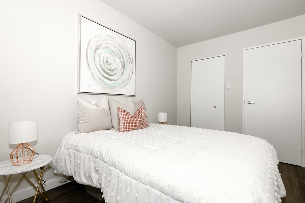A bedroom with a white bed and a large abstract painting above it.