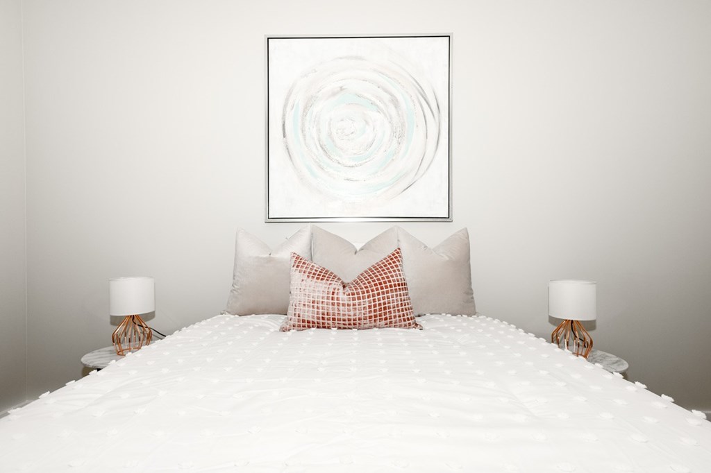 A bed with white bedspread and two pillows with a white and red checkered pillowcase.