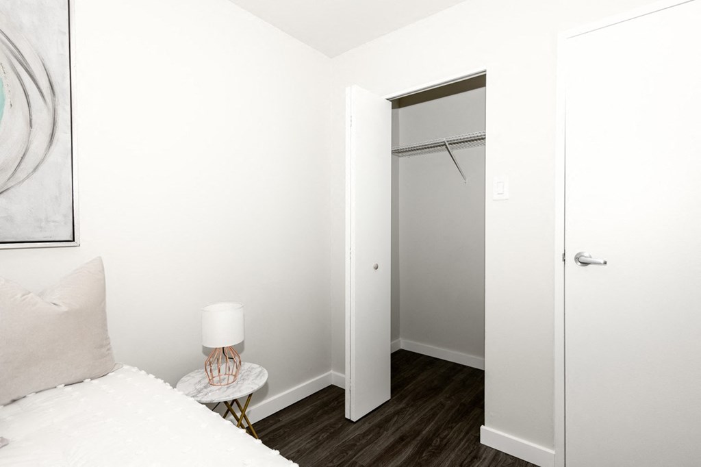 A white bedroom with a bed, nightstand, and closet.