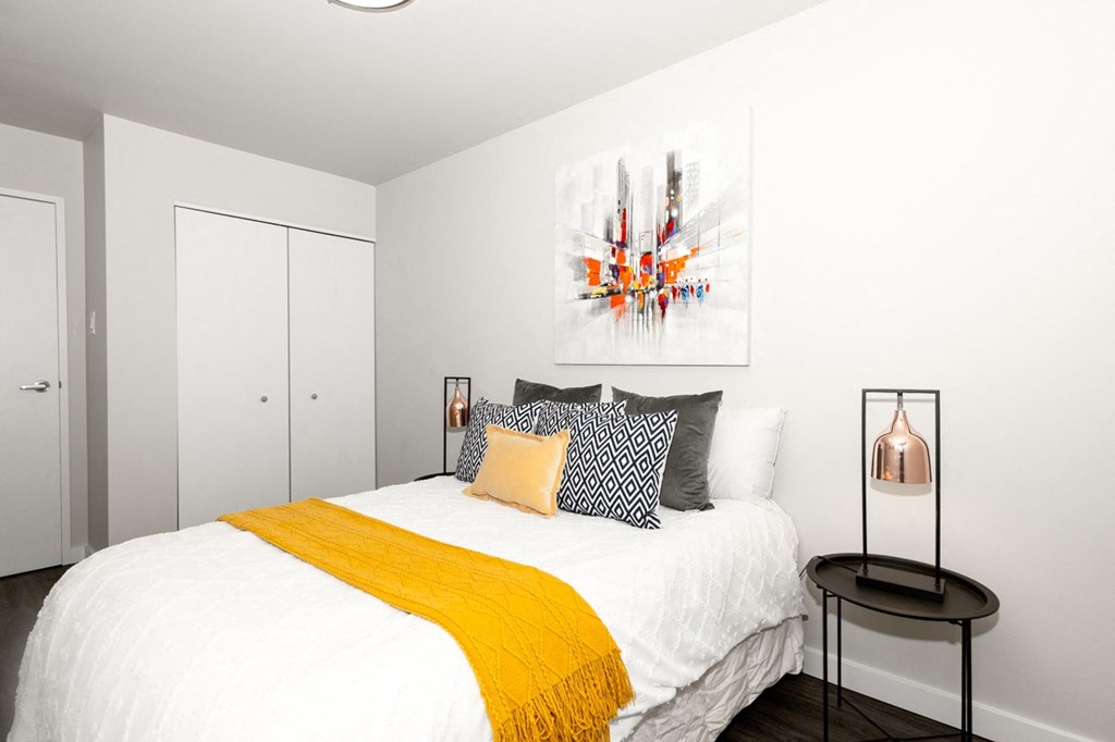 A bedroom with a bed, a yellow throw, and a painting on the wall.