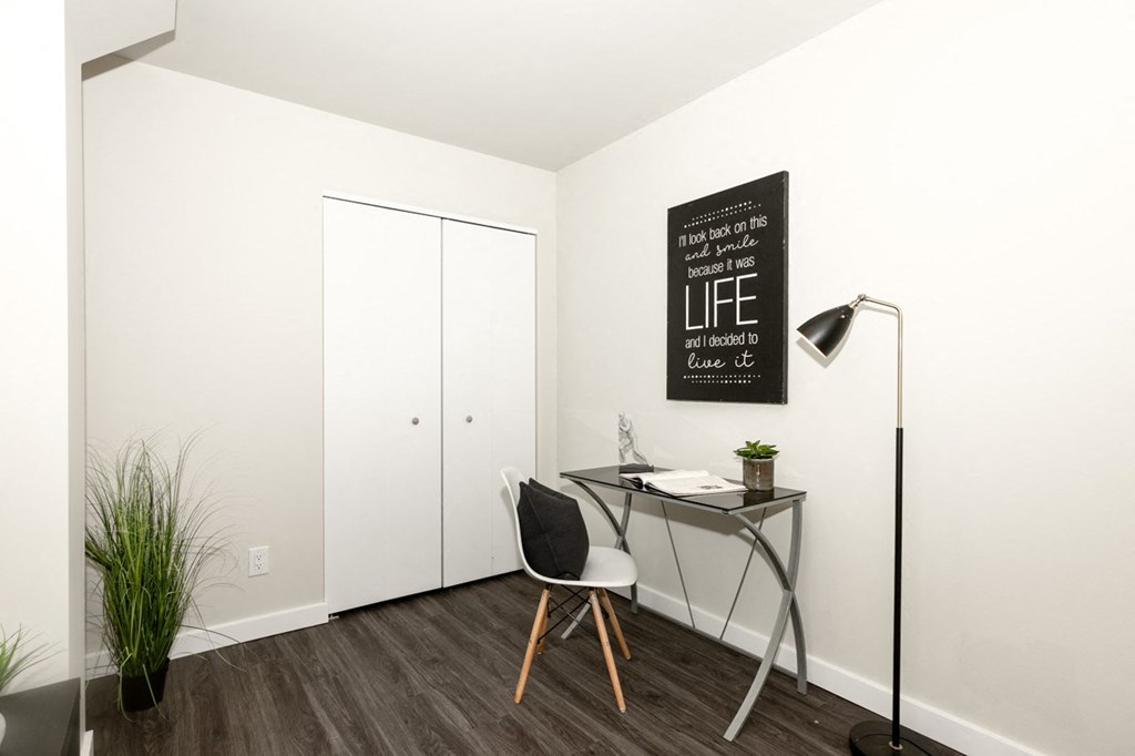 A black and white photo of a room with a desk and a chair.