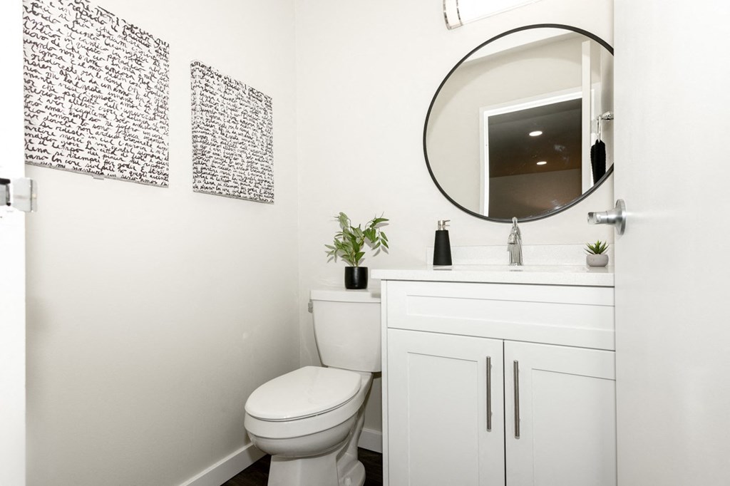 A white bathroom with a toilet, a mirror, and two wall hangings.