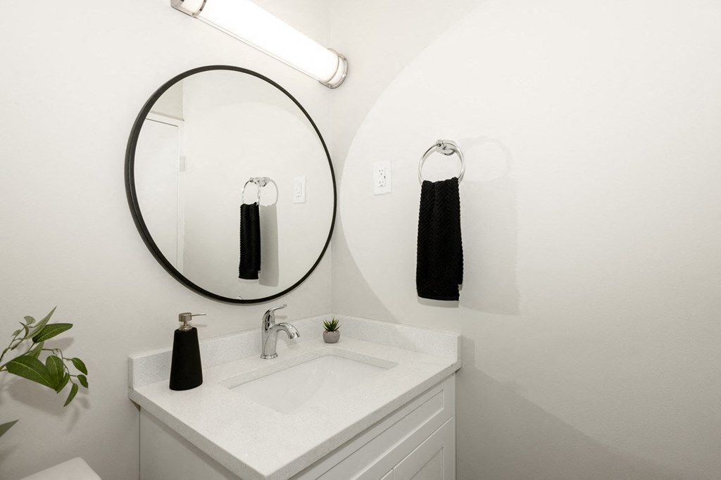 A bathroom with a white sink and a round mirror.