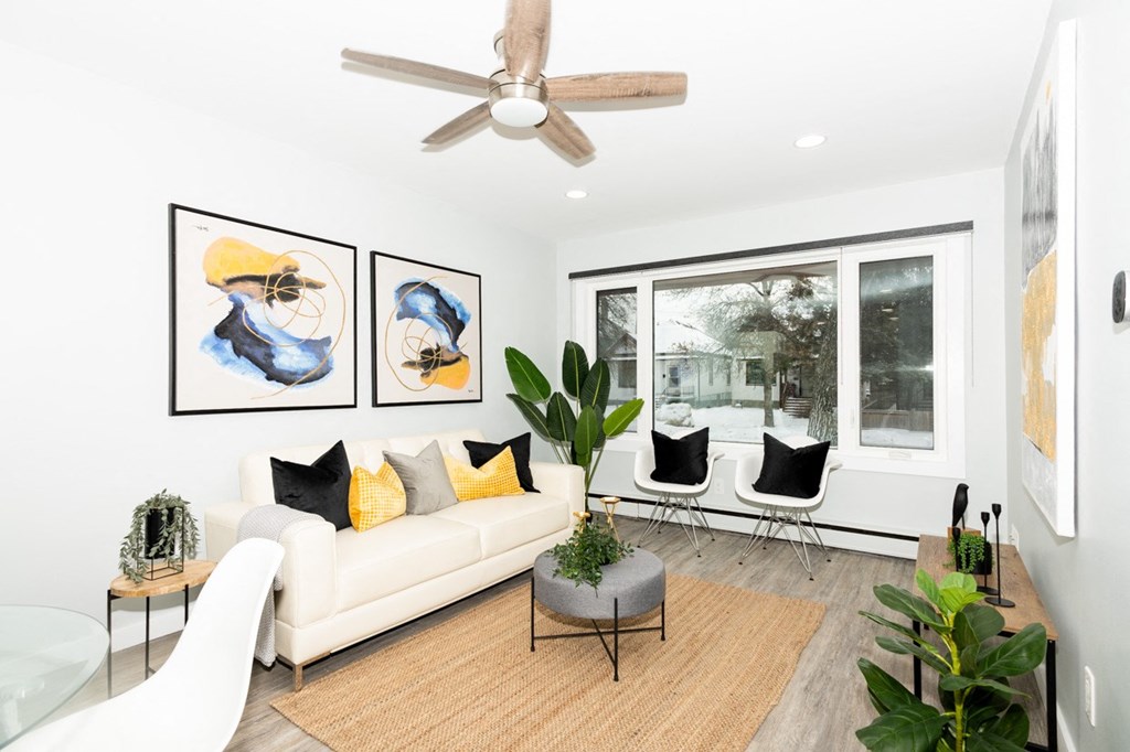 A living room with a white couch, two chairs, a coffee table, and a ceiling fan.