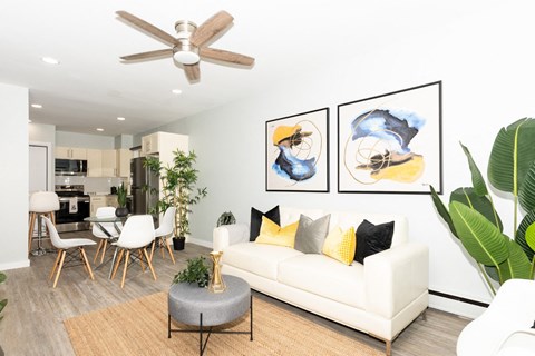 A living room with a white couch, a grey ottoman, and a ceiling fan.