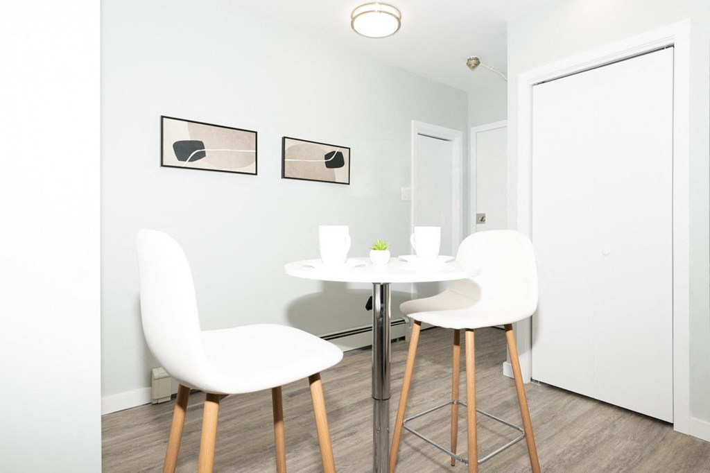 A white chair with wooden legs is in front of a white table with a cup and saucer on it.