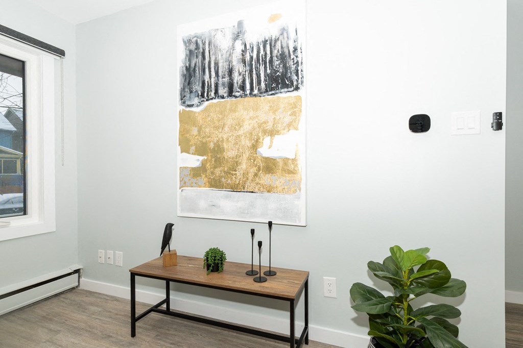 A painting of a forest with a gold area in the middle is hanging on a white wall.