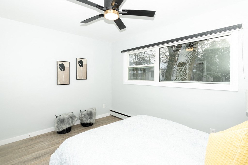 A bedroom with a bed, a window, a fan, and two pictures on the wall.