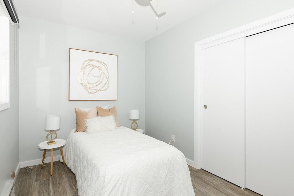 A bedroom with a white bed and a framed artwork on the wall.