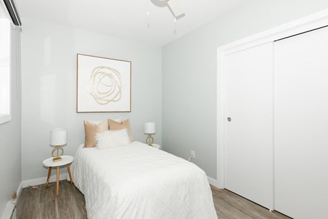 A bedroom with a white bed and a framed artwork on the wall.
