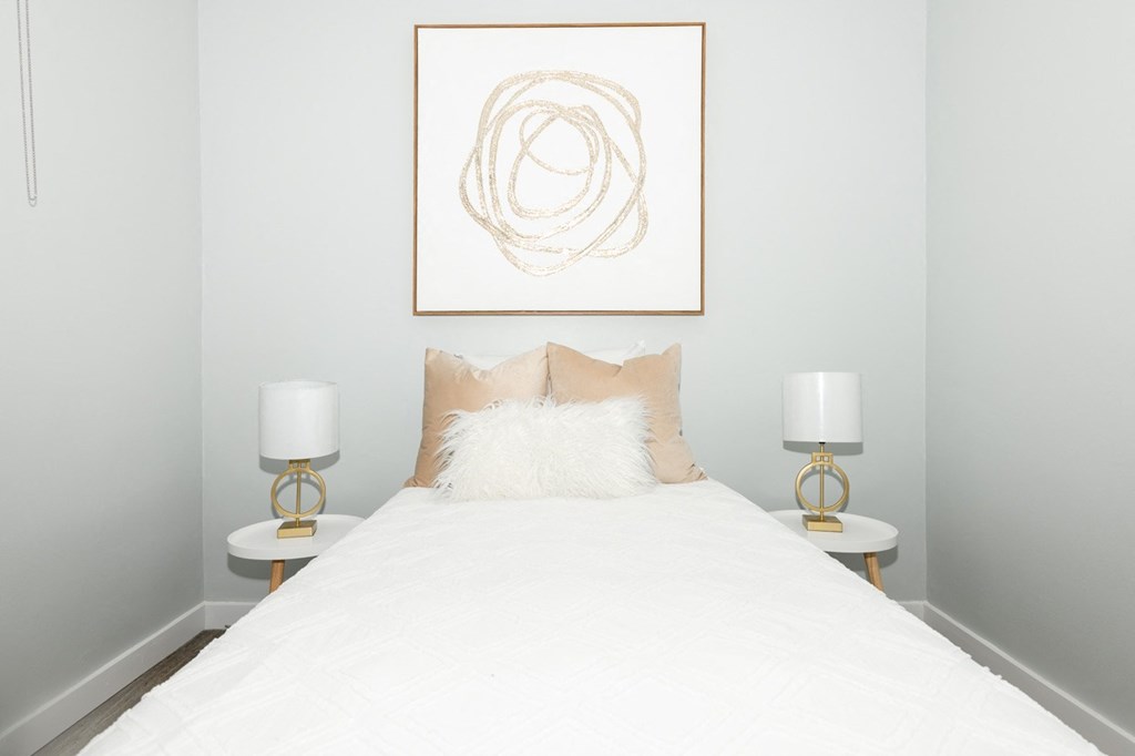 A bedroom with a white bed and two lamps on either side of the bed.