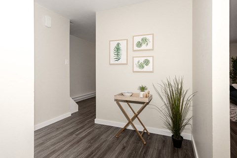 A room with a wooden floor and a white wall with three framed pictures hanging on it.