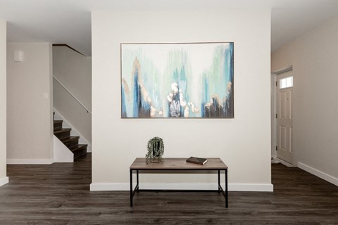 A painting hangs on the wall above a table with a cactus and a book on it.