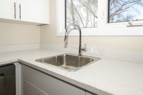 A kitchen sink with a faucet and a window in the background.