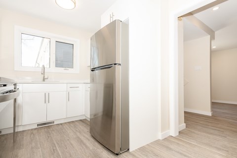 A stainless steel refrigerator stands in a kitchen with white cabinets and a window.