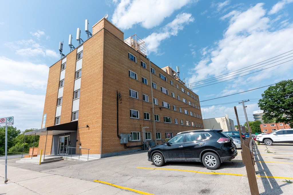 A black car is parked in a parking lot in front of a brick building.