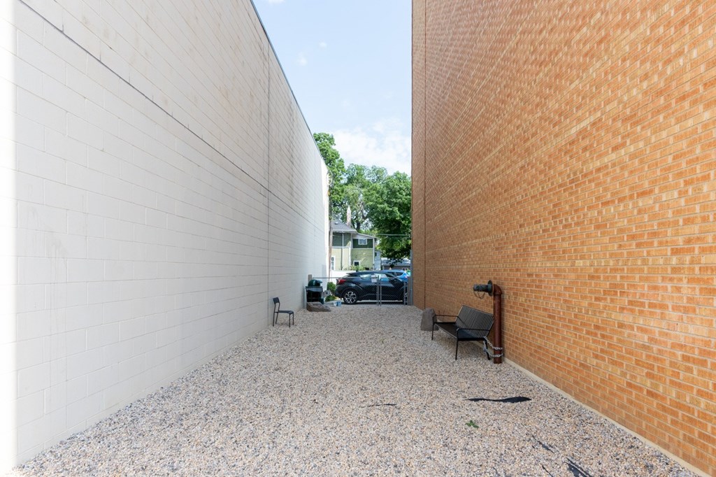 A gravel area between two buildings with a bench and a black bag on the ground.