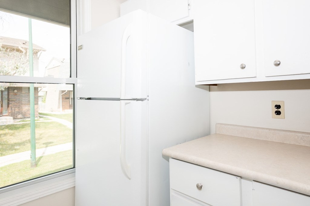 A white refrigerator in a kitchen with a window showing a view of a house and a lawn.