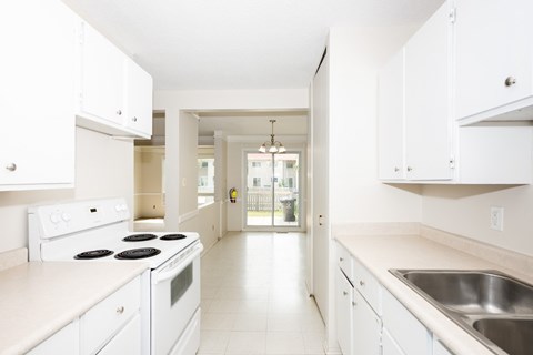 A white kitchen with a stove, sink, and cabinets.
