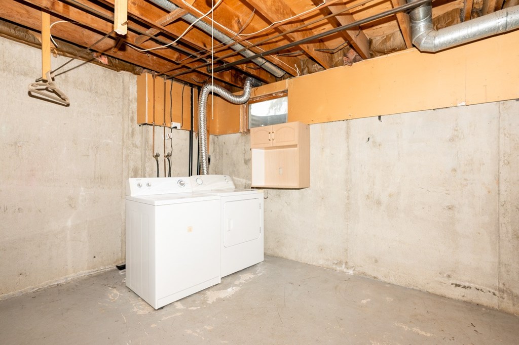 A white tank sits in a room under a ceiling with pipes.