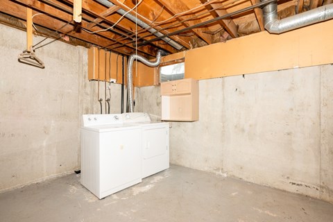 A white tank sits in a room under a ceiling with pipes.