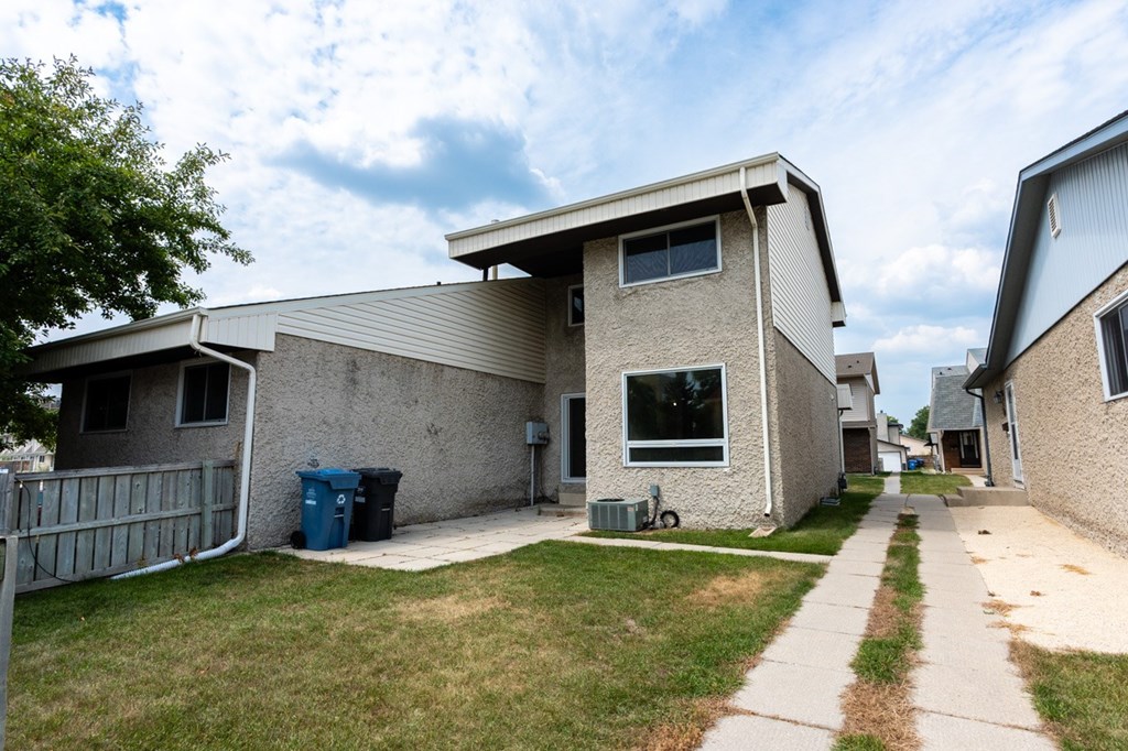 A house with a grey fence and a blue trash bin.