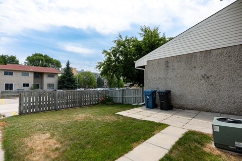 A backyard with a fence, a trash can, and a building in the background.