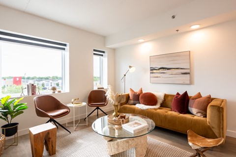 A living room with a brown sofa, a glass table, and a painting on the wall.