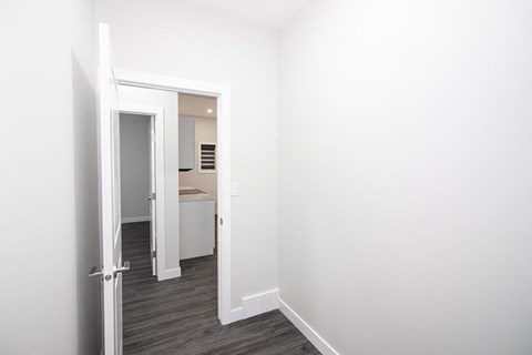 A white door is open to a small bedroom with a bed and a dresser.