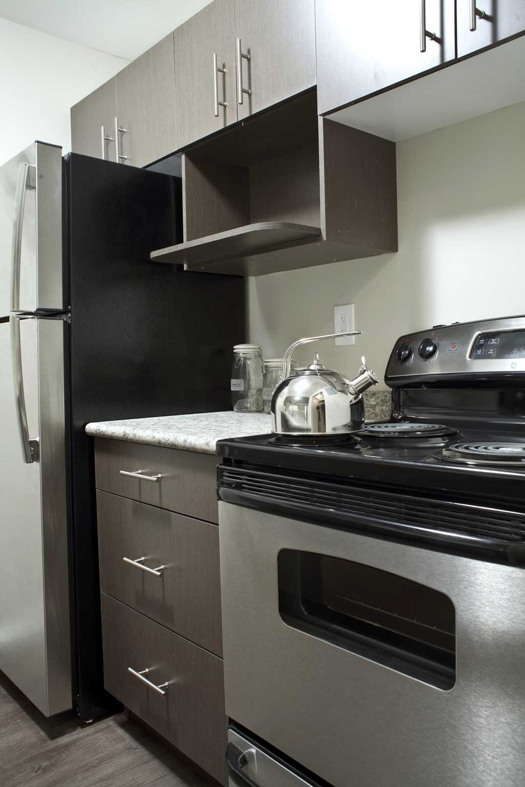 A modern kitchen with a black refrigerator, stainless steel oven, and a white countertop.
