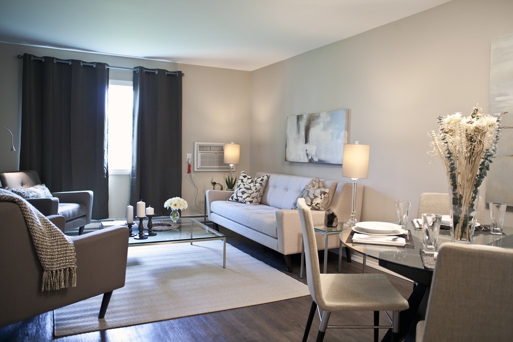 A modern living room with a grey sofa, a glass coffee table, and a large painting on the wall.