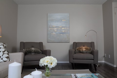 Two grey chairs with pillows and a painting on the wall.
